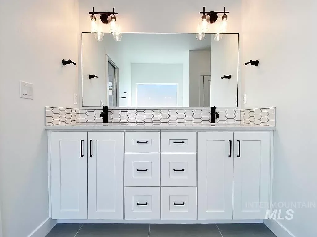 White vanity with full-height doors, hexagonal tile backsplash, dual sinks, and black hardware