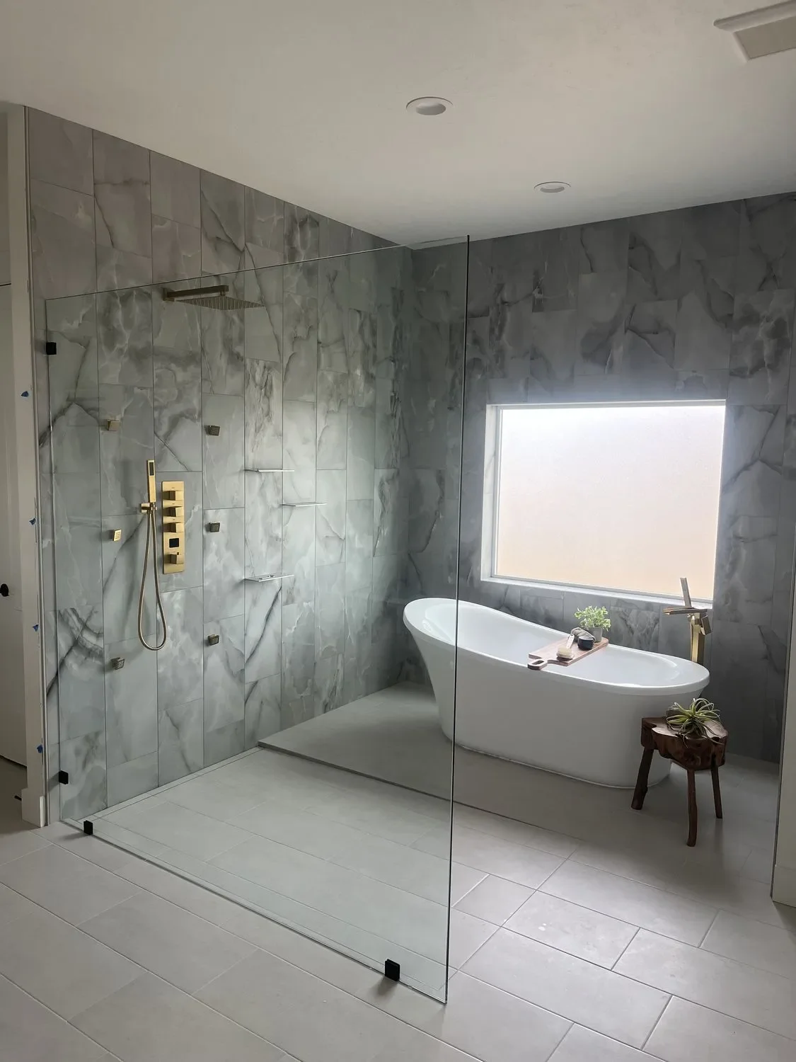 Marble tile bathroom with custom cabinetry, glass shower enclosure, and freestanding tub