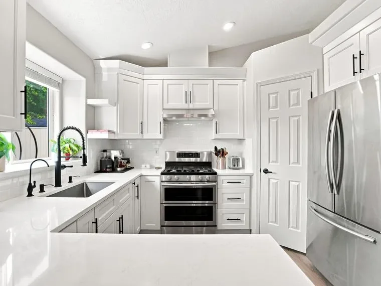 White shaker cabinets with black hardware, gas range, and stainless steel appliances in modern kitchen