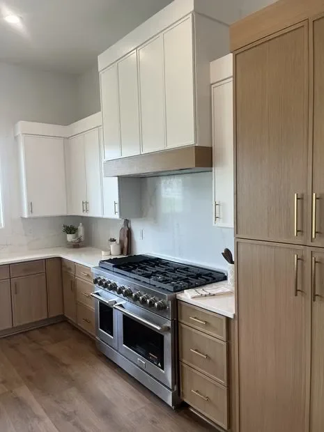 White and natural wood kitchen cabinets with stainless steel range hood and dual-oven gas cooktop