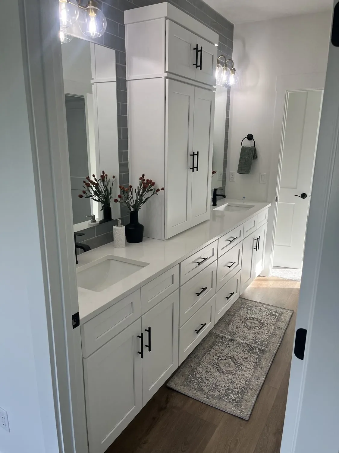 White shaker cabinetry with quartz countertop, framed mirror, and dark tile backsplash in master bathroom