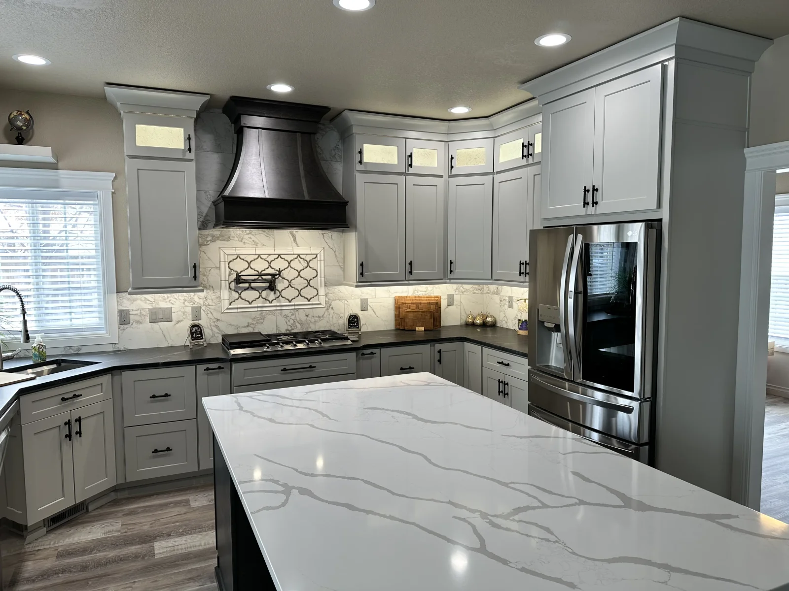 Gray shaker cabinets, marble backsplash, black range hood, quartz waterfall island