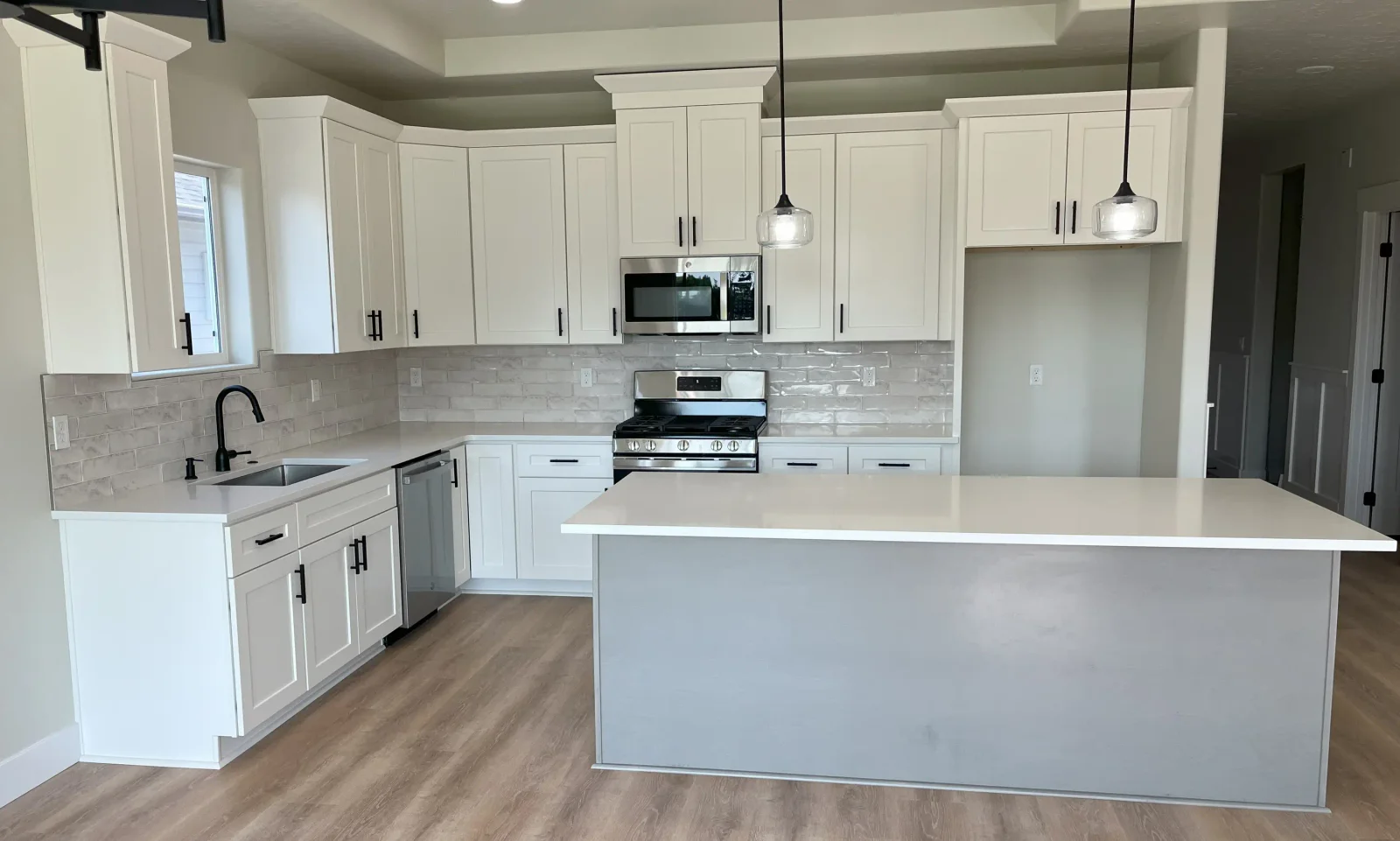 White shaker cabinets with black hardware, gray subway tile backsplash, large island with waterfall edge, stainless steel appliances